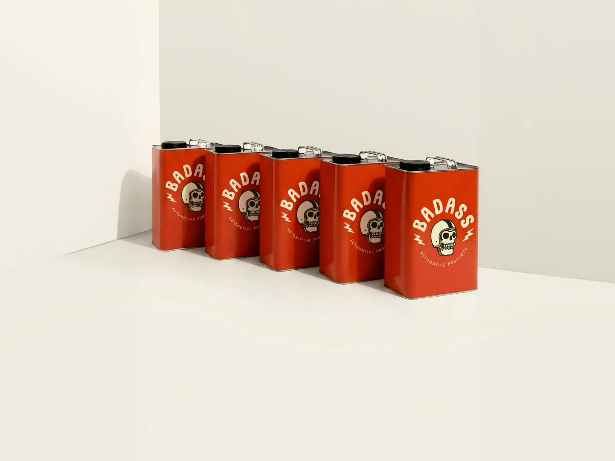 Five red BADASS-branded oil cans lined up against a white wall, each carrying the full medallion.